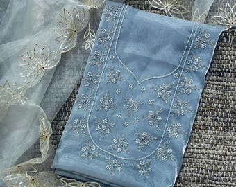 May include: A light blue organza fabric piece featuring intricate silver floral embroidery and beadwork along the neckline. The fabric is paired with a sheer white overlay adorned with metallic gold lotus-shaped cutouts along the scalloped edges.