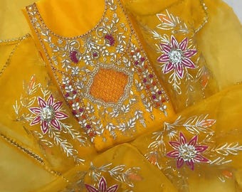 May include: A bright yellow garment featuring intricate silver embroidery and floral motifs with pink accents. The fabric displays a textured central panel surrounded by detailed metallic thread work and decorative embellishments throughout the piece.