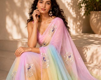 May include: A sheer, rainbow-colored sari with a gradient of pink, yellow, blue, and green. The sari is adorned with embroidered peacock motifs. The woman is wearing matching earrings and a pink top.