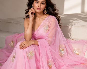 May include: A light pink saree with gold and silver floral embroidery. The sheer fabric drapes elegantly, creating soft folds. The saree is worn in a traditional style, with the pallu cascading over the shoulder.