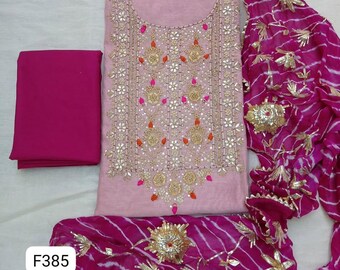 May include: A light pink tunic featuring intricate gold embroidery, sequins, and small pink and orange accents. It is paired with a solid magenta fabric piece and a magenta and white tie-dye scarf adorned with gold floral embellishments.