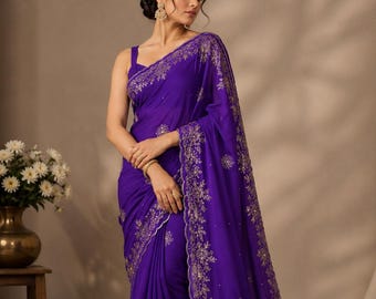 May include: A vibrant purple saree with intricate gold embroidery along the borders and neckline. The saree features a flowing design and is draped elegantly. The fabric appears to be a lightweight material, suitable for special occasions.