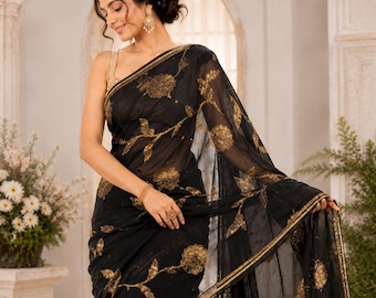 May include: Black sari with gold floral embroidery. The sheer fabric drapes elegantly, showcasing intricate golden flower and vine patterns. The sari features a gold border and is worn by a person.