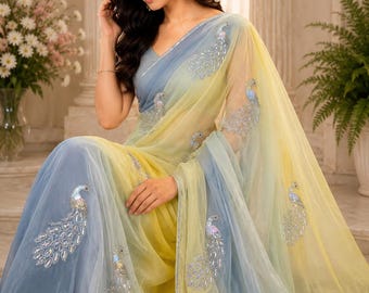 May include: A flowing, ombre saree in shades of yellow and blue, adorned with embroidered peacock motifs. The sheer fabric drapes elegantly, creating a soft, ethereal look. The saree features a V-neck design and is embellished with sparkling details.