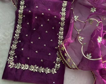 May include: A deep purple organza fabric garment featuring intricate gold-toned floral embroidery along the rectangular border and scattered small floral accents across the center, paired with a matching sheer purple dupatta.