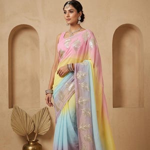 May include: A multi-coloured saree in pastel shades of pink, yellow, blue, and purple. The saree has gold leaf embroidery on the edges and bodice. The garment is worn by a person, set against a neutral beige backdrop.