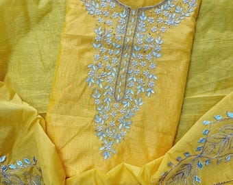 May include: A bright yellow fabric garment featuring intricate silver embroidery and reflective mirror-like embellishments arranged in floral and leaf patterns around the neckline and along the hemline, creating a detailed decorative design.