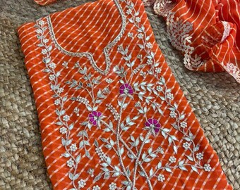 May include: An orange and white striped tunic featuring a notched neckline and intricate embroidery. The design includes silver leaf-shaped accents, small white floral beads, and vibrant magenta circular flower centers across the front panel.