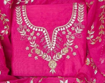 May include: A vibrant fuchsia fabric piece featuring intricate gold-toned embroidery and metallic leaf-shaped accents around the neckline. The material has a subtle textured weave, and the surrounding sheer fabric displays a repeating vine pattern.