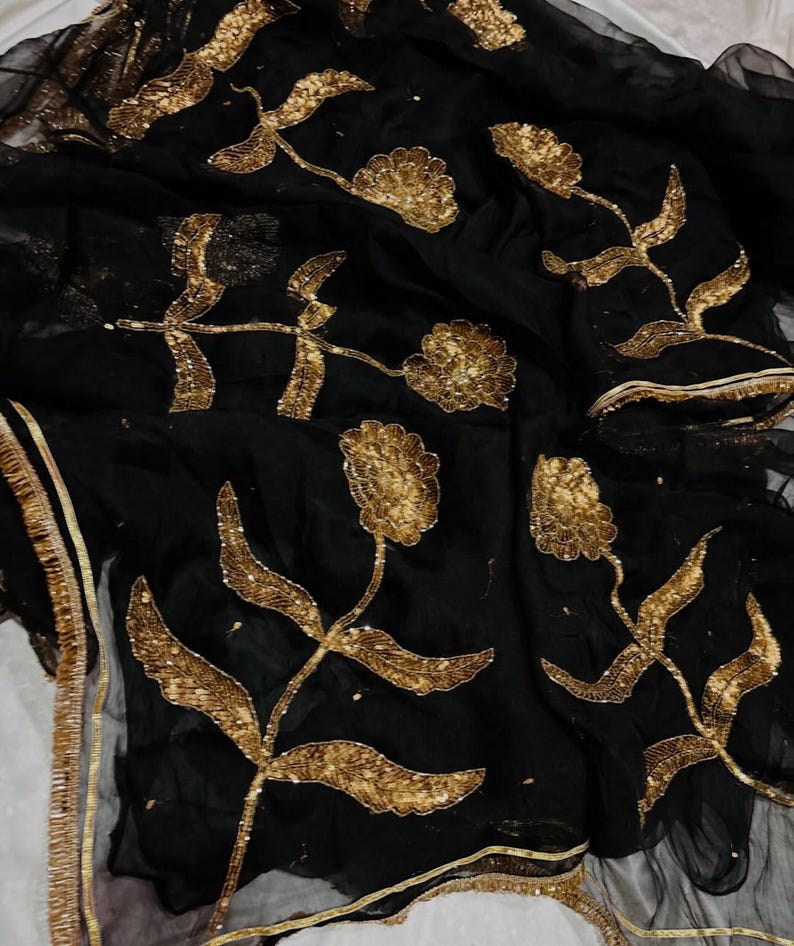 May include: Black fabric with gold floral embroidery. The design features detailed gold flowers and leaves, with gold trim along the edges. The fabric appears to be sheer, with a delicate texture.
