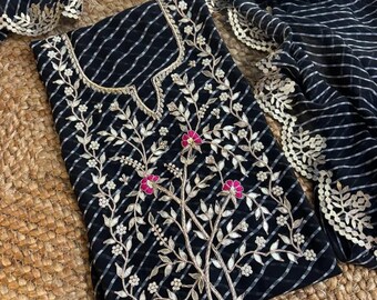 May include: A black tunic featuring a white diagonal striped pattern and intricate embroidery of silver leaves and bright pink flowers. The neckline is trimmed with gold piping, and the garment is paired with a matching black striped scarf with white lace trim.