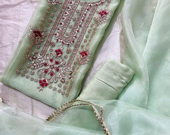 May include: A light mint green semi-sheer tunic featuring intricate silver metallic embroidery and small red floral accents along the neckline and front panel. The garment is paired with a matching mint green scarf with a decorative silver trim.