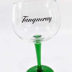 Może przedstawiać: Przezroczysty kieliszek do ginu z zieloną n&oacute;żką i podstawą. Na szkle czarnym skryptem wydrukowano słowa "Tanqueray". Kieliszek przeznaczony jest do koktajli i innych napoj&oacute;w.