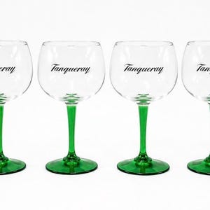 Może przedstawiać: Sześć przezroczystych kieliszk&oacute;w do ginu z zielonymi n&oacute;żkami i podstawami. Na każdym kieliszku czarnym drukiem napisano słowo "Tanqueray". Kieliszki ustawione są w rzędzie na białym tle.