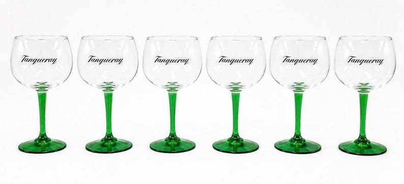 Może przedstawiać: Sześć przezroczystych kieliszk&oacute;w do ginu z zielonymi n&oacute;żkami i podstawami. Na każdym kieliszku czarnym drukiem napisano słowo "Tanqueray". Kieliszki ustawione są w rzędzie na białym tle.