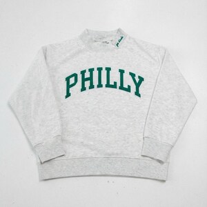 May include: A light gray heathered long-sleeve sweatshirt featuring the word PHILLY in large, dark green, arched block letters across the chest. The mock neck collar includes the small embroidered green text go birds on the left side.