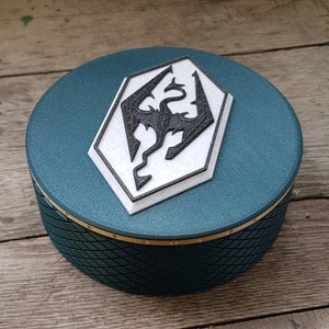 May include: A teal round box with a black and white dragon symbol on the lid. The box has a textured pattern on the sides.