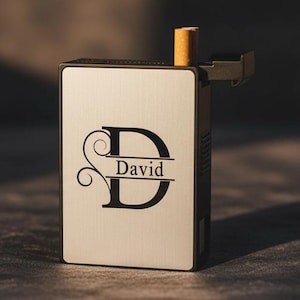 May include: A personalized cigarette case with the name "David" printed on the front. The case is rectangular, with a light-colored front and a black border. A single cigarette is visible at the top.
