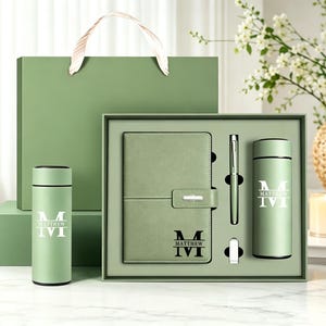 May include: A sage green gift set featuring a notebook, a pen, and two insulated tumblers. The notebook and tumblers are personalised with the name Matthew and a large letter M. The set is presented in a matching green box and gift bag.
