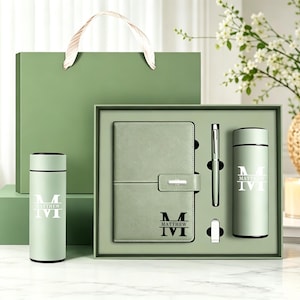 Può includere: Un set regalo color verde salvia composto da un taccuino con chiusura magnetica, una penna in metallo e due borracce cilindriche termiche. Ogni articolo è personalizzato con la lettera M e il nome Matthew in una stampa grafica.