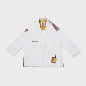 May include: A white martial arts gi jacket featuring a Garfield graphic on the lower front, a green Garfield patch on the shoulder, and a yellow and black striped inner collar lining. The text "ALBINO & PRETO" is embroidered in green on the chest.