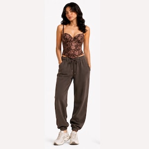 May include: A brown floral corset top with thin straps and a sweetheart neckline. The top is paired with brown sweatpants with a drawstring waist and elastic cuffs. The outfit is completed with white sneakers.