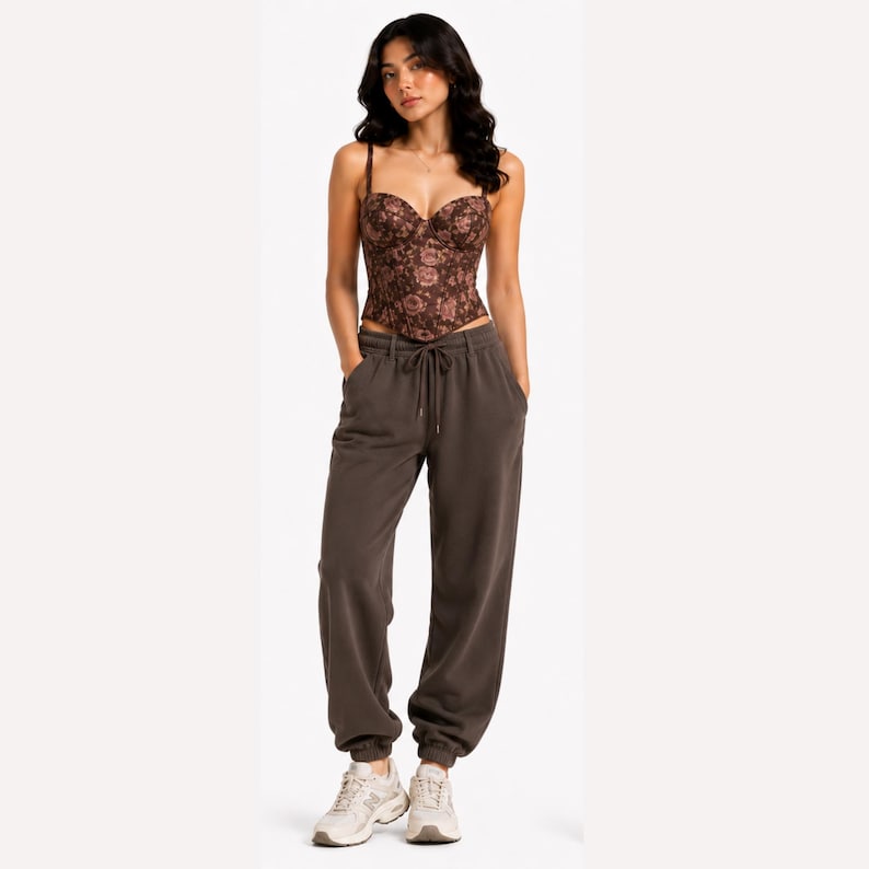 May include: A brown floral corset top with thin straps and a sweetheart neckline. The top is paired with brown sweatpants with a drawstring waist and elastic cuffs. The outfit is completed with white sneakers.