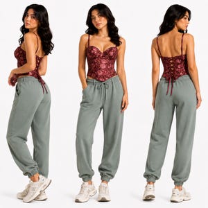 May include: A burgundy floral print corset top with spaghetti straps and a lace-up back. Paired with sage green sweatpants with a drawstring waist and elastic cuffs. The outfit is completed with white sneakers.