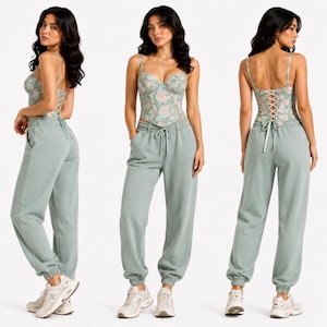 May include: A three-panel image shows a floral print corset top with spaghetti straps and a lace-up back, paired with matching sage green sweatpants. The corset features a light green background with pink floral patterns. The sweatpants have a drawstring waist and cuffed ankles.