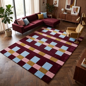 Peut inclure: Un tapis rectangulaire présentant une couleur de base bordeaux profond avec un motif géométrique de carrés et de rectangles répétés en bleu clair, jaune moutarde et rose pâle, créant un design en grille structuré sur toute la surface.