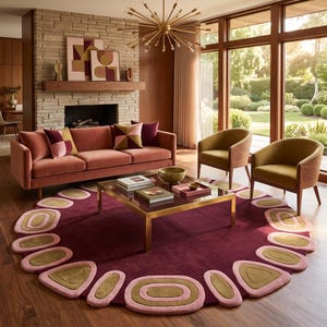 May include: A large circular rug in deep burgundy featuring a border of repeating oval and triangular shapes in soft pink and olive green. The rug is placed on a wooden floor beneath a square glass coffee table with a gold metal frame.