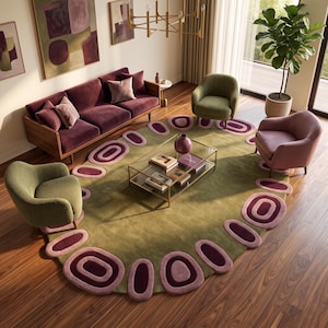 May include: An oval area rug featuring a solid olive green center with a border of concentric purple and pink oval shapes. The rug is placed in a living room with a velvet sofa, two green armchairs, one pink armchair, and a glass coffee table.