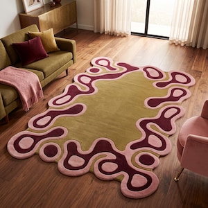 May include: A rectangular area rug featuring a solid olive green center surrounded by an irregular, organic border pattern in shades of deep burgundy and soft pink. The rug has a tufted texture and a non-uniform, wavy edge design.