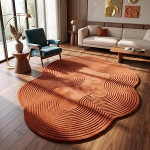 May include: An irregular, organic-shaped area rug in a deep burnt orange color. The rug features a textured surface with concentric, raised circular lines that ripple outward from two central points, creating a topographic, wave-like pattern.