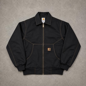 May include: A black zip-up jacket featuring a pointed collar, long sleeves with ribbed cuffs, and a ribbed hem. The garment is constructed with contrasting brown stitching, a central brass-toned zipper, and a rectangular Carhartt brand patch.
