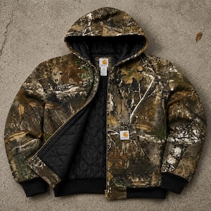 May include: A Carhartt hooded jacket featuring a camouflage pattern in shades of brown, green, and tan. The jacket has a black quilted lining, a front zip closure, black ribbed cuffs and hem, and a Carhartt brand patch on the front pocket.