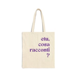 May include: A cream-colored tote bag with purple text that reads "etu, cosa racconti ?". The bag has a rectangular shape with a handle, suitable for carrying items. The text is in a sans-serif font.