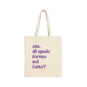 May include: A cream-colored tote bag with purple text that reads "etu, di quale forma sei fatto?" The bag has two handles and is made of a sturdy fabric. The text is centered on the front of the bag.
