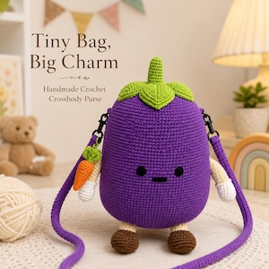 May include: A handmade crochet crossbody purse shaped like a purple eggplant with a green stem, small black eyes, a flat mouth, beige arms with white hands, and brown feet. A small orange carrot charm hangs from the purple strap.