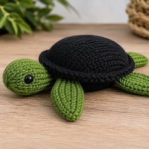 Op de afbeelding: Een handgemaakt gehaakt schildpadspeeltje met een effen zwart schild en een gestructureerde groene kop en flippers. De schildpad heeft een klein, rond, zwart plastic oog aan de zijkant van de kop, met een gedetailleerd gebreid steekpatroon.