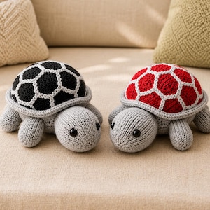 May include: Two crocheted turtle toys with light gray bodies and black plastic eyes. One turtle features a black shell with white hexagonal outlines, while the other has a red shell with white hexagonal outlines. Both have gray flippers.