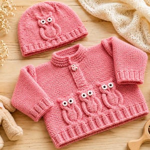 Könnte beinhalten: Ein Set aus einer rosa Strickjacke und einer passenden Mütze mit erhabenen Eulenmotiven und weißen Knopfaugen. Die Strickjacke hat lange Ärmel, einen gerippten Kragen und einen Knopfverschluss, während die Mütze einen gerippten Saum aufweist.