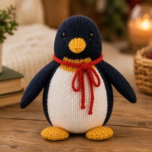 Può includere: Un peluche a forma di pinguino lavorato a maglia a mano con testa e schiena blu scuro, pancia bianca e piedi e becco giallo brillante. Il pinguino ha due piccoli occhi neri e indossa una sottile sciarpa rossa lavorata a maglia annodata al collo.