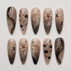 Può includere: Un set di dieci unghie finte a mandorla con una base sfumata dal nude al grigio scuro. I disegni includono viticci in rame metallizzato, zucche nere, fantasmi bianchi, lune crescenti, fiori a cinque petali e stelle dorate con piccoli borchie.