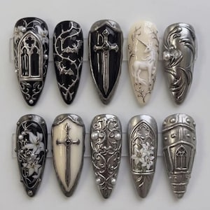 May include: A set of ten press-on nails featuring intricate 3D designs in black, white, and metallic silver. The nails display motifs including gothic arches, bats, swords, a unicorn, floral lily patterns, and ornate filigree with small pearls.
