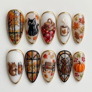 May include: A set of ten almond-shaped press-on nails featuring autumn-themed designs including a black cat, a picnic basket, a steaming mug, falling leaves, a squirrel with a thermos, a park bench, a stained-glass cat, and an orange pumpkin.