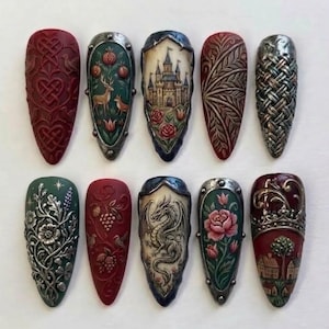 May include: Ten decorative nail art tips arranged in two rows. Each tip features intricate 3D relief designs including a castle, a dragon, floral patterns, a deer, a fox, a woven metal texture, and a landscape scene with houses in various colors.