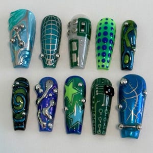 May include: A set of ten press-on nails featuring various designs in shades of blue, green, and silver. The nails include patterns such as grids, stars, circuit board lines, and abstract swirls, accented with small, raised silver metallic spheres.