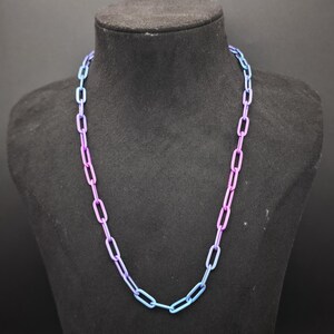 May include: A chain necklace featuring elongated rectangular links with a smooth finish. The metal links display a gradient color transition, shifting from a vibrant blue at the top and bottom to a deep purple hue along the center sections of the chain.