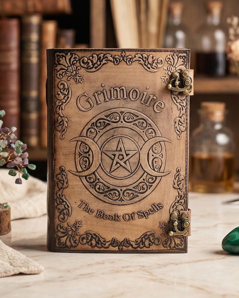 K&ouml;nnte beinhalten: Ein braunes, ledergebundenes Buch mit dem gepr&auml;gten Wort "Grimoire" auf dem Einband. Der Einband zeigt ein Pentagramm in einem Kreis und Halbmonde. Der Text "The Book Of Spells" ist ebenfalls sichtbar. Das Buch hat Metallverschl&uuml;sse.